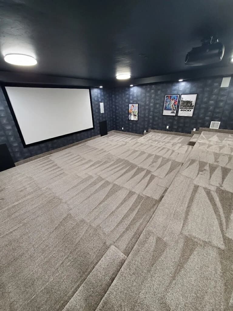 Tiered carpet, a projection screen, and a ceiling-mounted projector in a finished basement room.
