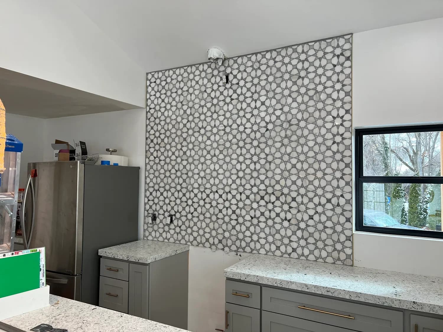 Patterned black-and-white tile feature wall, gray cabinets, fridge, in progress