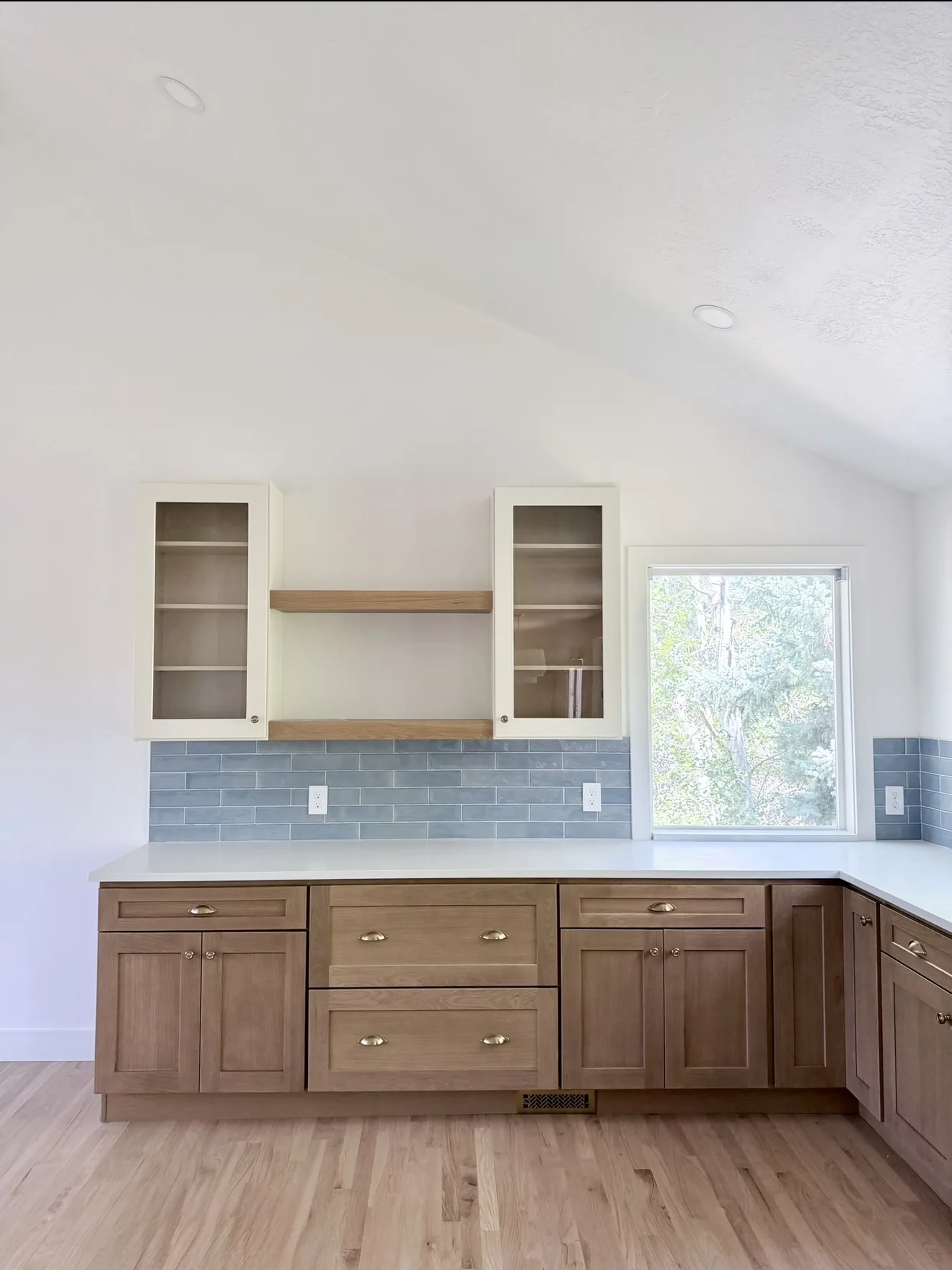 Oak lower cabinets, white glass uppers, blue subway tile, and gold hardware under a vaulted ceiling