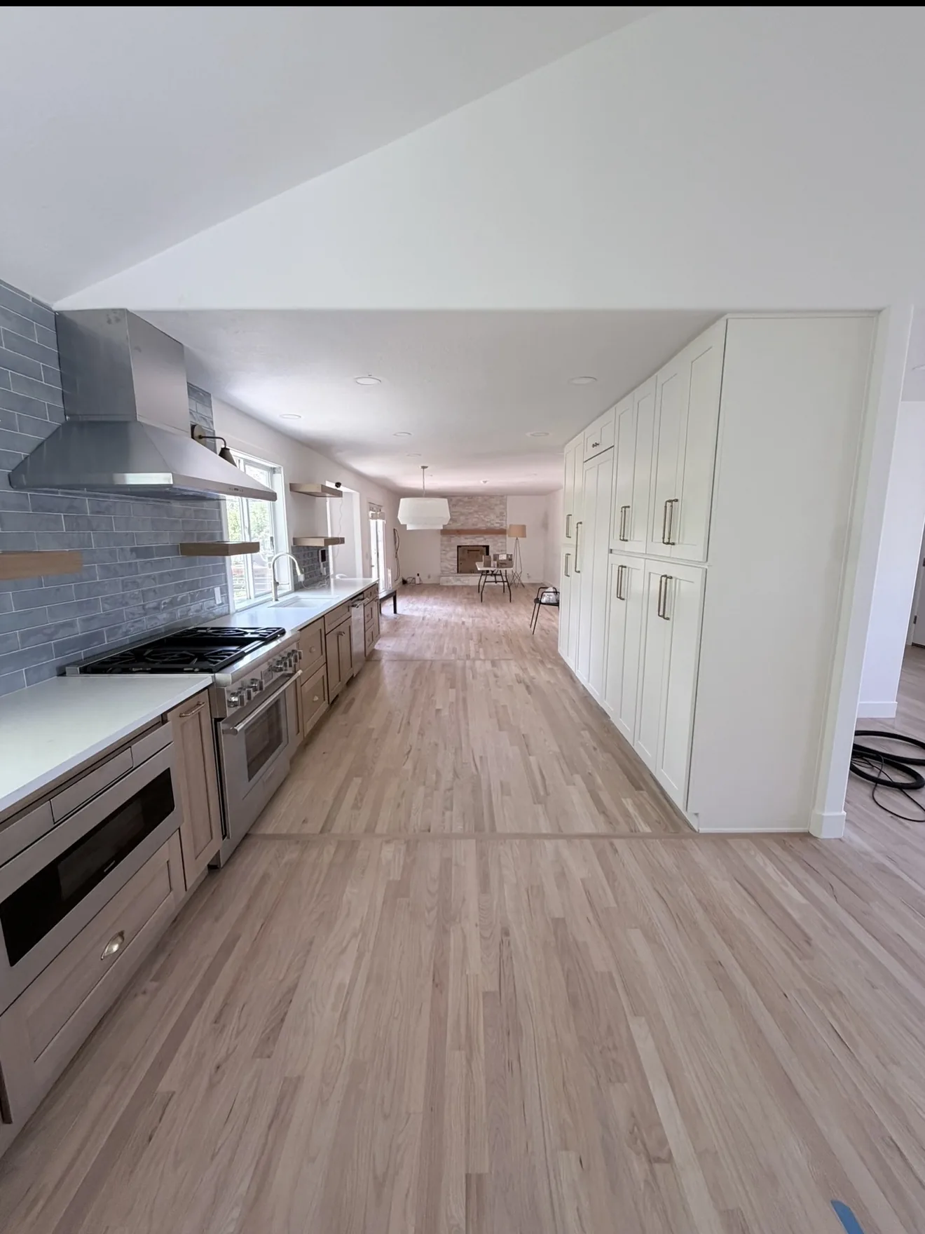 Oak and white kitchen with a stainless range, blue tile, and the next room still open