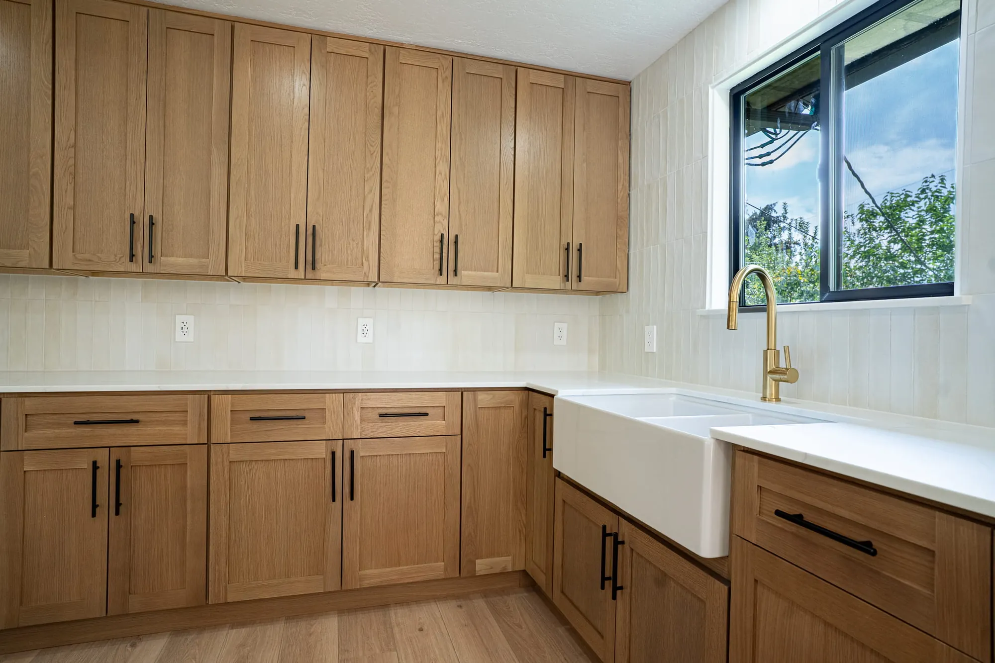 White-oak cabinets, white farmhouse sink, brass faucet, black window