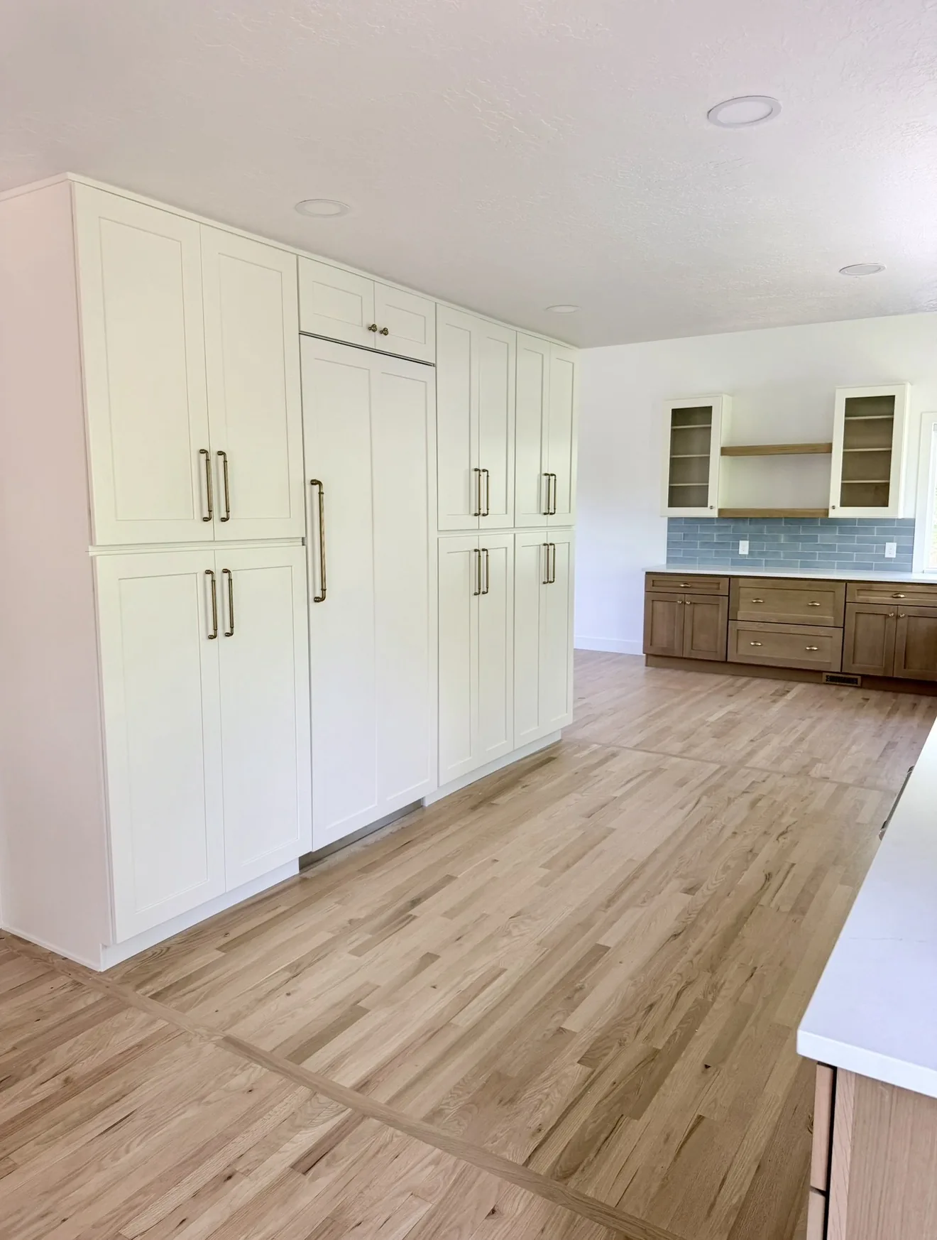 White pantry cabinets with gold pulls beside oak lowers and a blue tile backsplash